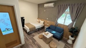 A room with a bed, a blue sofa, a small table, a plant, and an air conditioning unit. - TS Hotel (Taitung)