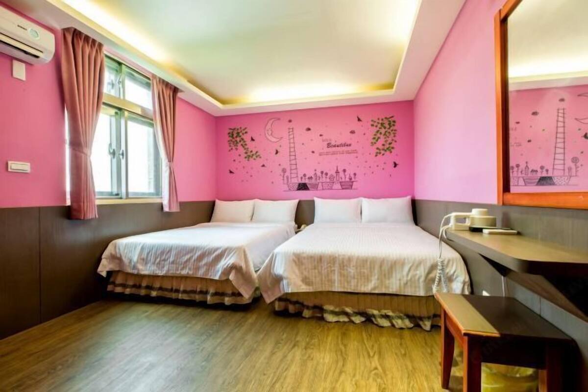 A room with two beds, a desk, and a window with curtains.