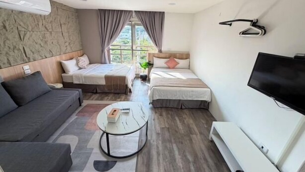 A hotel room with a sofa, two beds, a TV, and a window with curtains. - TS Hotel (Taitung)