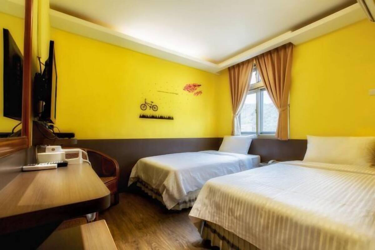 A hotel room with two beds, a desk, a chair, a TV, and a window with curtains.