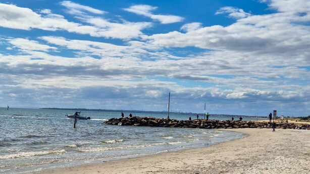 Une plage avec une digue rocheuse, une mer calme et un ciel dégagé.