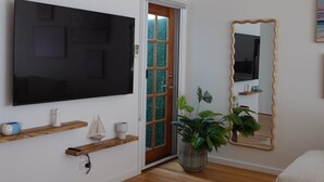 Un salon doté d’un téléviseur à écran plat, d’étagères en bois, d’une table basse blanche, d’une plante en pot et d’un miroir.