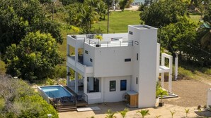 Un bâtiment moderne à deux étages, doté d’une piscine, entouré de verdure et offrant une vue sur la mer.