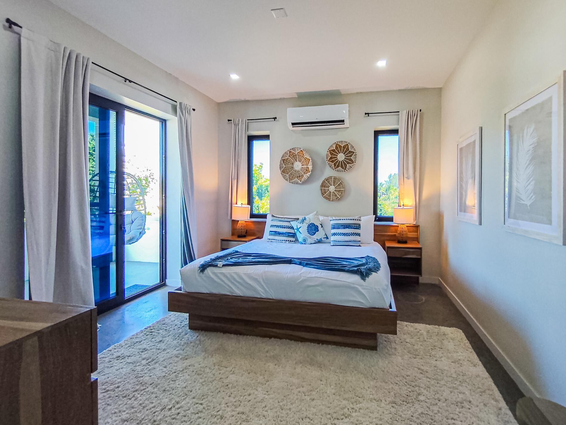 A bedroom with a bed, a large window, an air conditioning unit, and a view of the outdoors.