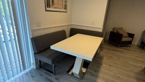 A room with a white table and bench, a ceiling fan, and a window with blinds. - Penguins on the Beach | 2BR Steps to Beach & Downtown w/pool | Unit 1 (Cocoa Beach)