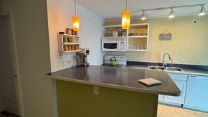 A compact kitchen with a central island, pendant lighting, and a microwave. - Penguins on the Beach | 2BR Steps to Beach & Downtown w/pool | Unit 1 (Cocoa Beach)