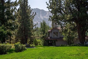 A single-story house with a sloped roof, surrounded by a well-maintained lawn and tall pine trees. - Tranquil & Woodsy 2/2 Retreat – Jacuzzi, W/D, BBQ! (Mammoth Lakes)