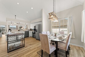 A modern kitchen with a dining area, featuring a glass table, chairs, and a hanging light fixture.