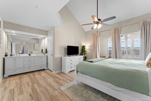 A bedroom with a bed, a TV, a ceiling fan, and a large window with curtains.