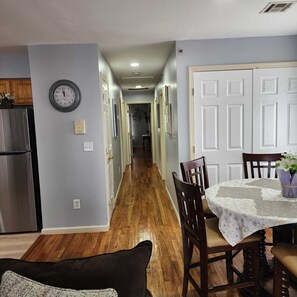 A hallway with a wooden floor, a dining area with a table and chairs, and a clock on the wall. - Spacious 6BR Newark Retreat near Penn Station - Free Parking-Sleeps 16+ (Newark)