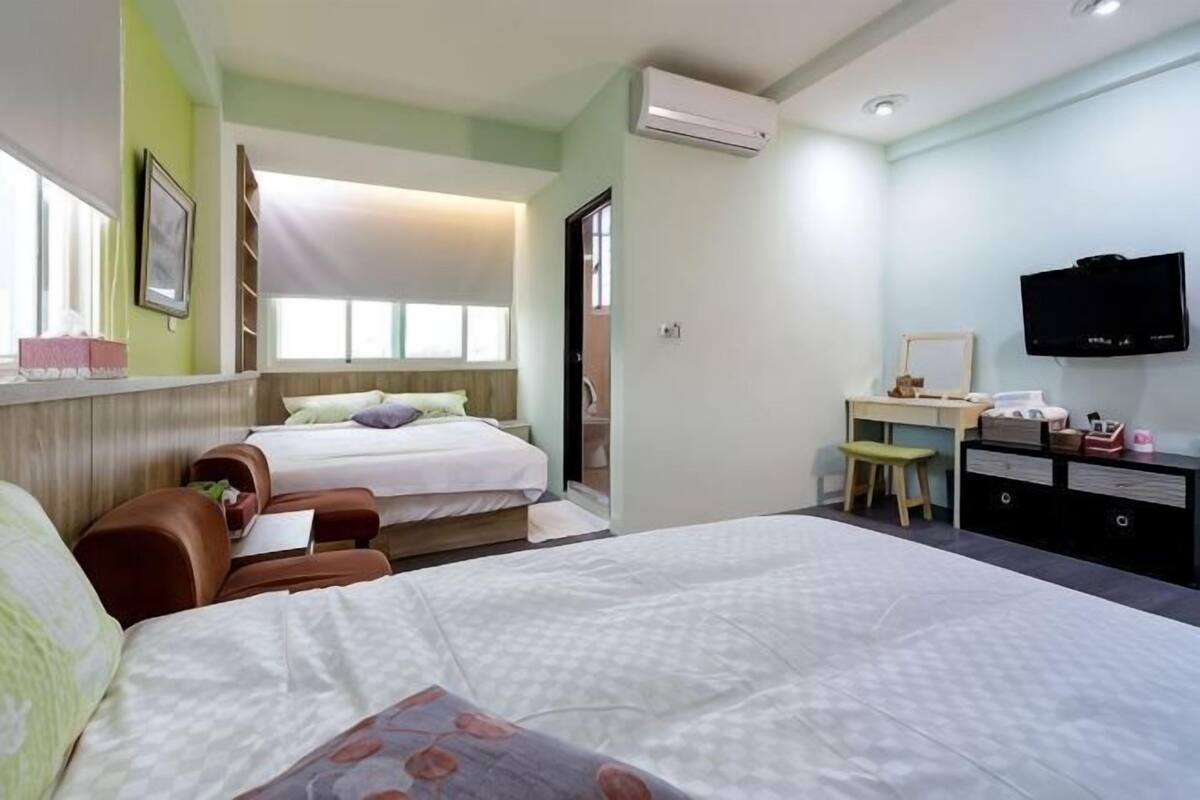 A hotel room with two beds, a desk, a chair, a television, and a window.