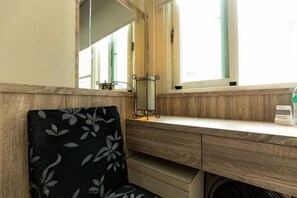 Een kamer met een houten bureau, een stoel met bloemenprint, een spiegel en een raam met jaloezieën.
