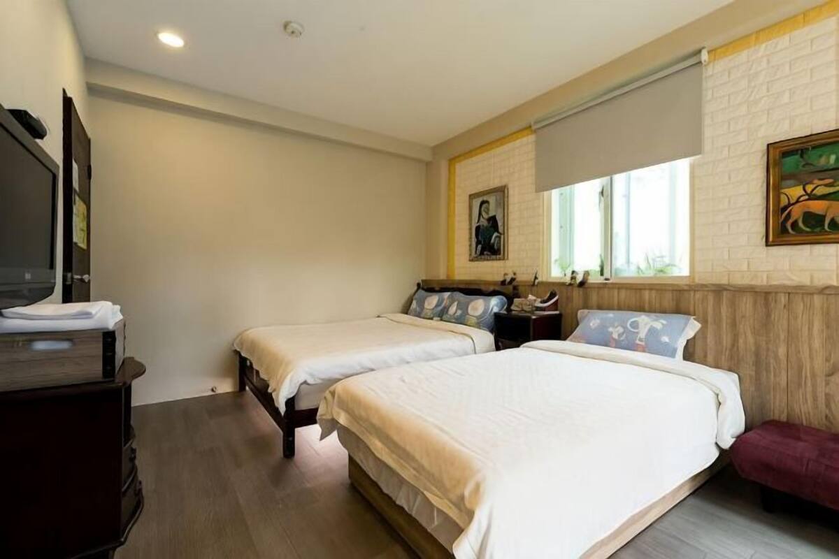 A hotel room with two beds, a TV, a window, and a painting on the wall.