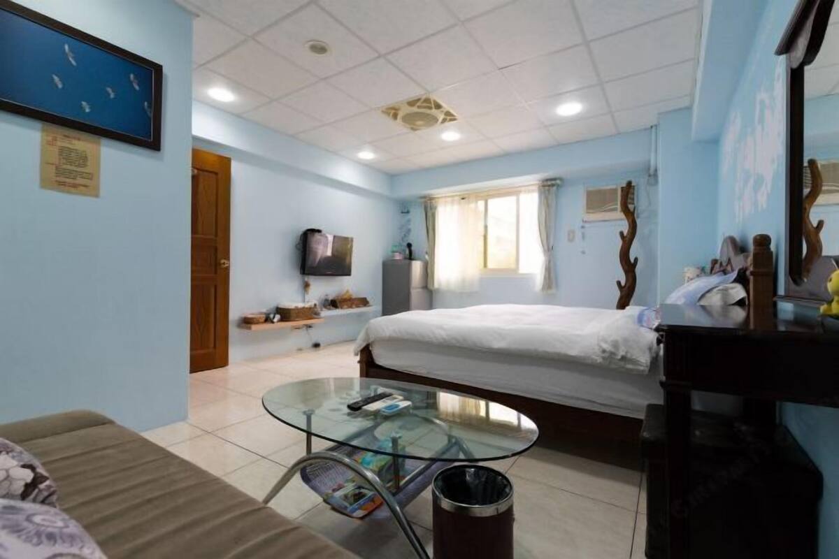 A hotel room with a bed, a glass table, a sofa, a TV, and a window with curtains.