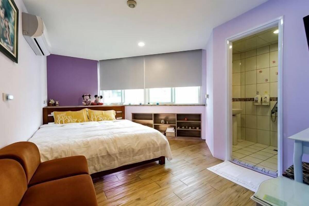A bedroom with a bed, a sofa, a walk-in closet, and a shower area.