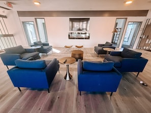Een moderne loungehoek met blauwe banken, een klein rond tafeltje en een open haard.