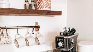 Una cucina con una macchina da caffè, una tazza, un piatto con una ciambella e un espositore a parete per tazze.