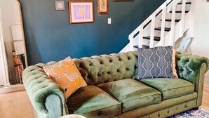 Un divano componibile verde con cuscini decorati, una lampada da terra in fibra naturale e un grande tappeto decorativo.
