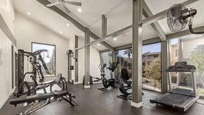 Una palestra moderna con diverse attrezzature per esercizi, ampie finestre e una ventola a soffitto.