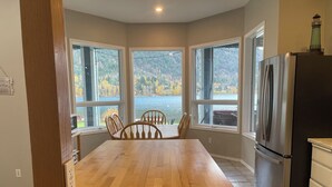 A kitchen with a wooden table, chairs, a refrigerator, and large windows overlooking a lake. - Lakefront Retreat 2 bedroom sleeps 6,  private hot tub and beach. (Nelson)