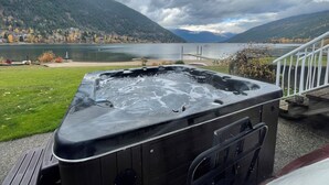A hot tub on a deck with a view of a lake and mountains. - Lakefront Retreat 2 bedroom sleeps 6,  private hot tub and beach. (Nelson)