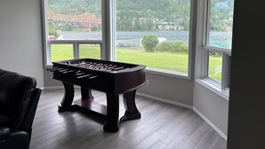 A foosball table in a corner with large windows overlooking a lake and a bridge. - Lakefront Retreat 2 bedroom sleeps 6,  private hot tub and beach. (Nelson)