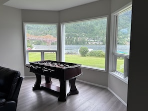 A foosball table in a corner with large windows overlooking a lake and a bridge.