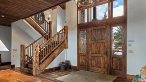 A spacious interior with a wooden staircase, large wooden doors, and a view of the outdoors. - Fore Seasons Lodge | Pole Creek Golf Course | Private Hot Tub | Sleeps 16! (Tabernash)