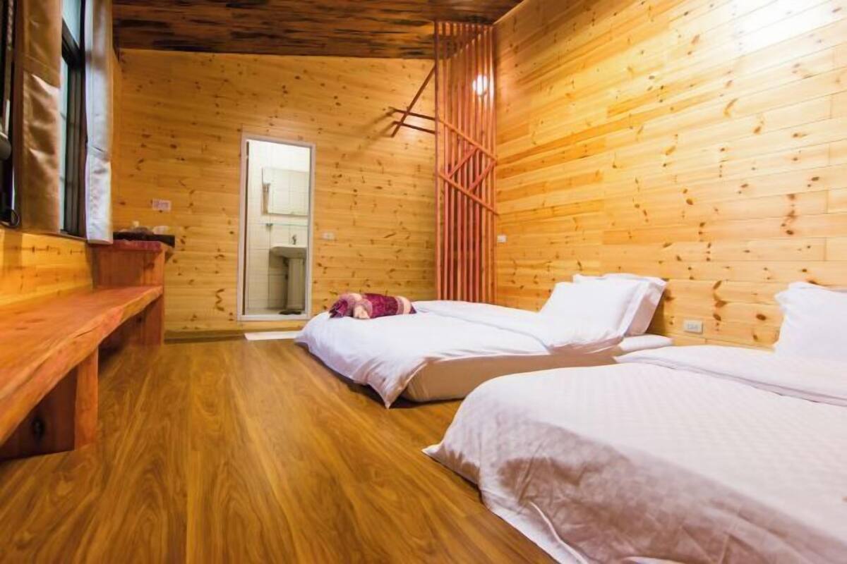 A wooden cabin with two beds, a bench, and a bathroom visible through a glass door.