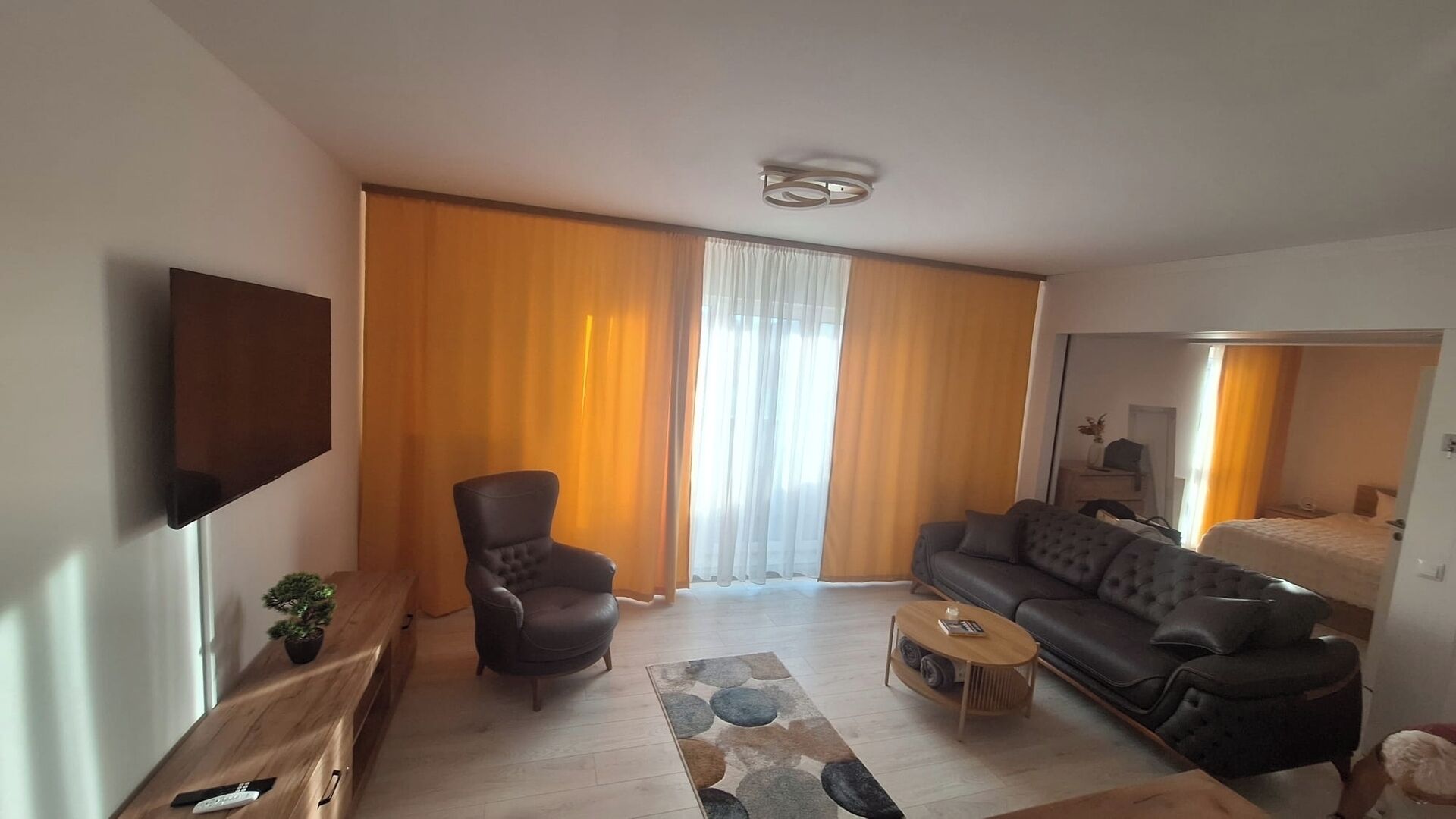 Een moderne woonkamer met een bank, fauteuil, salontafel en een aan de muur bevestigde televisie.