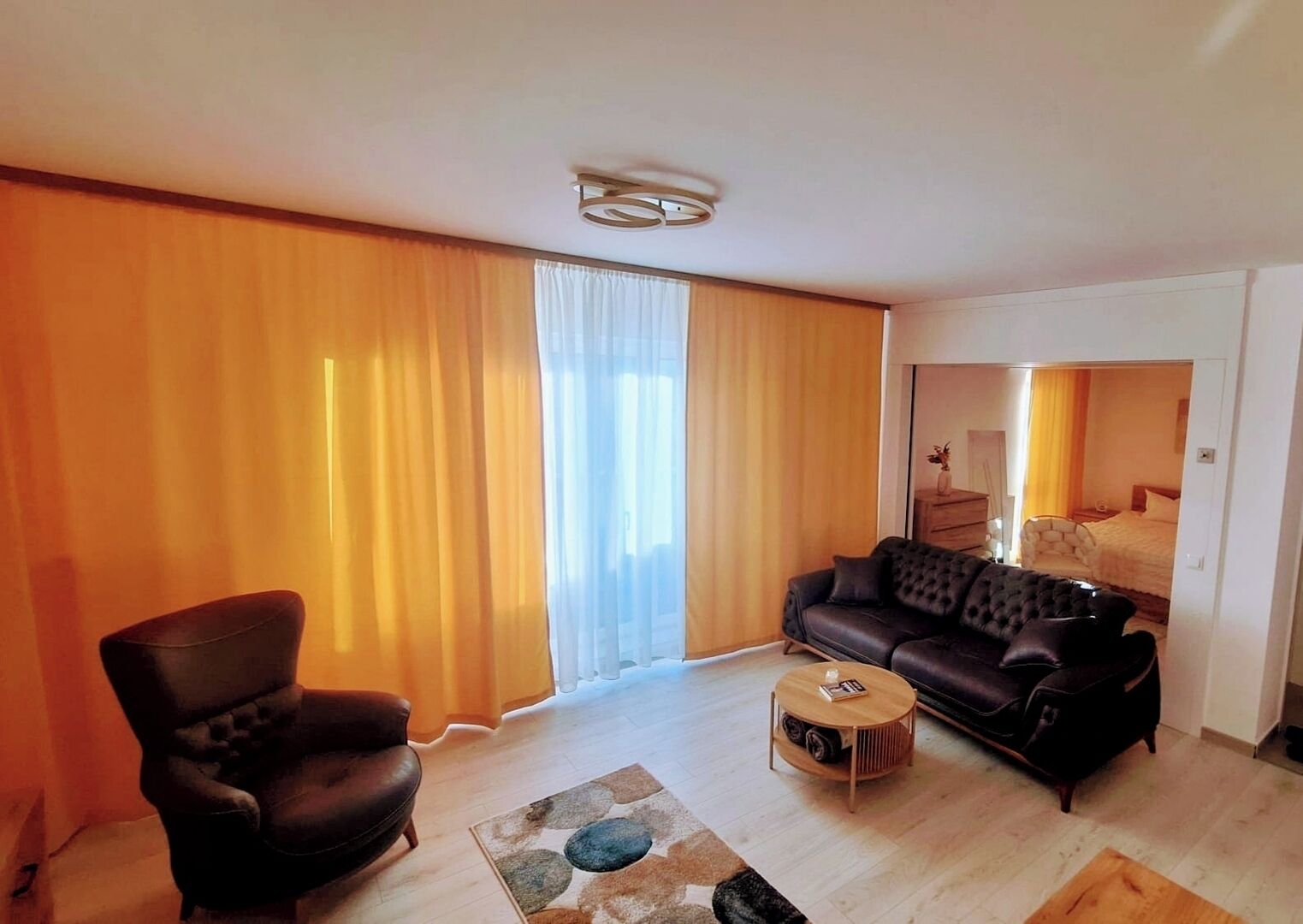 Uma sala de estar moderna com um sofá de couro, uma mesa de centro de madeira e uma grande janela com cortinas.