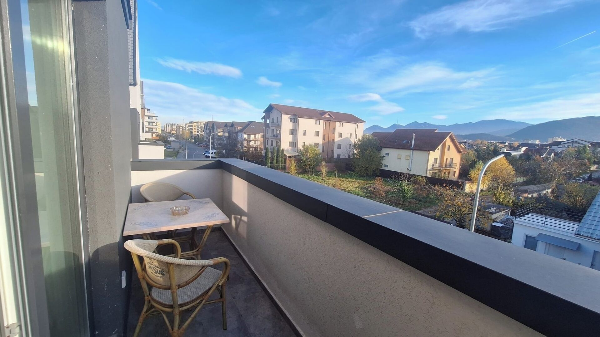 Een balkon met een tafel en stoelen, met uitzicht op een woonwijk met huizen en bergen op de achtergrond.