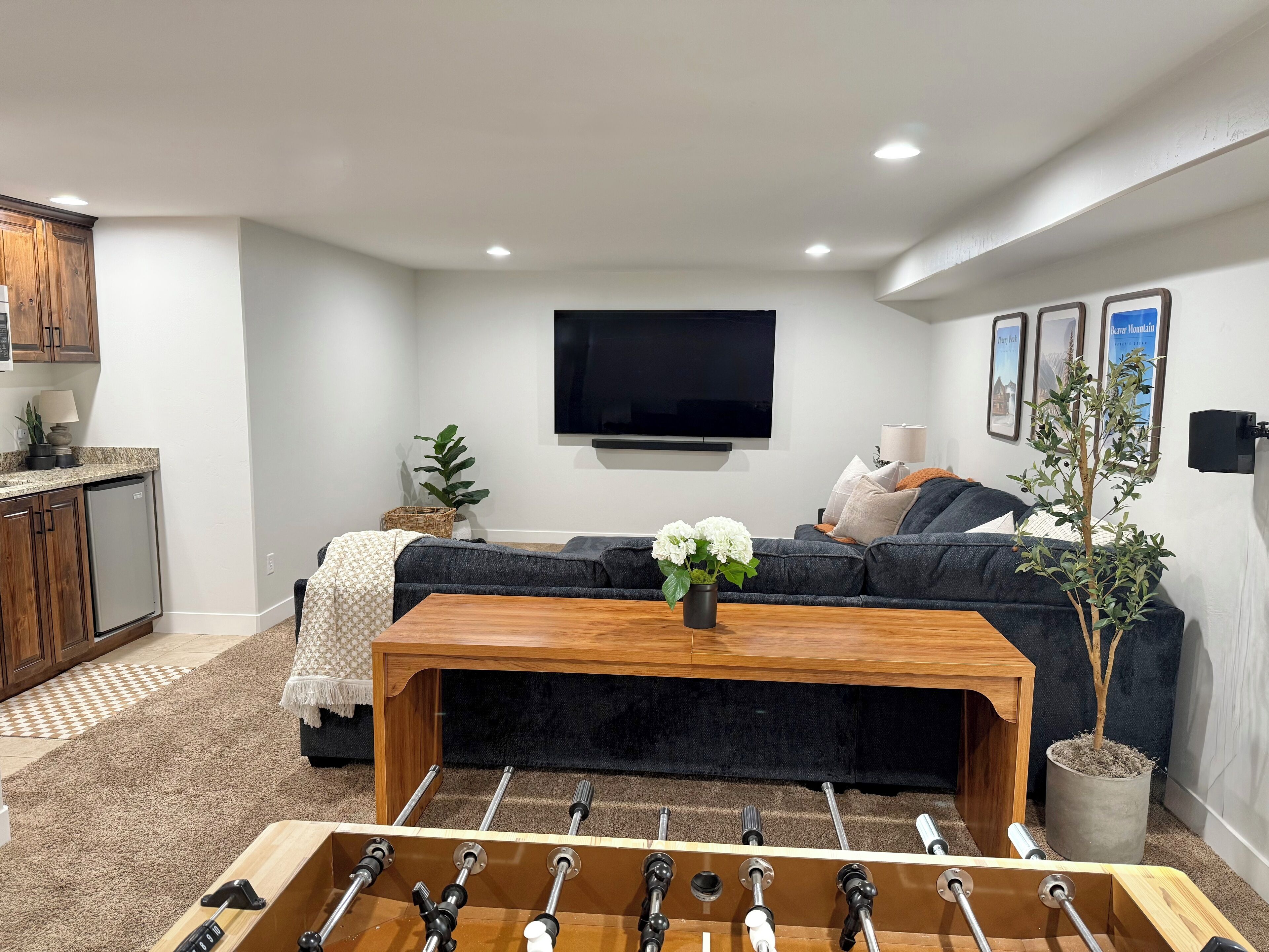 A modern living room with a sofa, a coffee table, a television, and a foosball table.