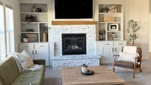A living room with a stone fireplace, a flat-screen TV, and built-in shelving. - Spacious retreat, sleeps 18 guests comfortably, theater and game room  (Smithfield)