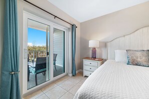 A bedroom with a bed, a nightstand, a lamp, a chair, and a sliding glass door leading to a balcony. - Ground-Floor Retreat | Steps to Beach, Pool & Fitness Center | BEACHBALL PROPERTIES (Orange Beach)