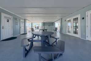 A covered outdoor area with a picnic table and benches, light blue walls, and doors leading to other areas. - Ground-Floor Retreat | Steps to Beach, Pool & Fitness Center | BEACHBALL PROPERTIES (Orange Beach)