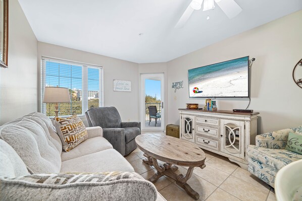 A living room with a sofa, armchair, coffee table, and a TV on a wall. - Ground-Floor Retreat | Steps to Beach, Pool & Fitness Center | BEACHBALL PROPERTIES (Orange Beach)