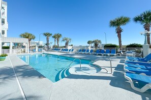 A pool area with blue lounge chairs and palm trees. - Ground-Floor Retreat | Steps to Beach, Pool & Fitness Center | BEACHBALL PROPERTIES (Orange Beach)