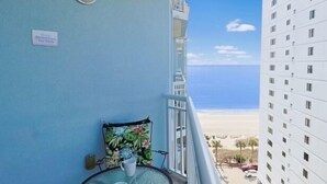 A balcony with a view of the beach, a small table with a chair, and a sign on the wall. - Stunning 10th-Floor 1-Bedroom Oceanview Condo (Myrtle Beach)