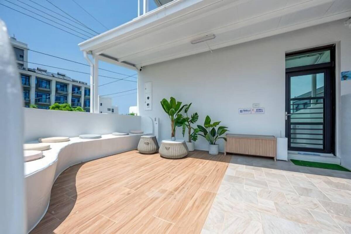 A modern outdoor area with a curved seating arrangement, potted plants, and a door with a sign.