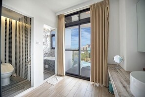 Un baño con ducha, inodoro y un ventanal grande con cortinas.