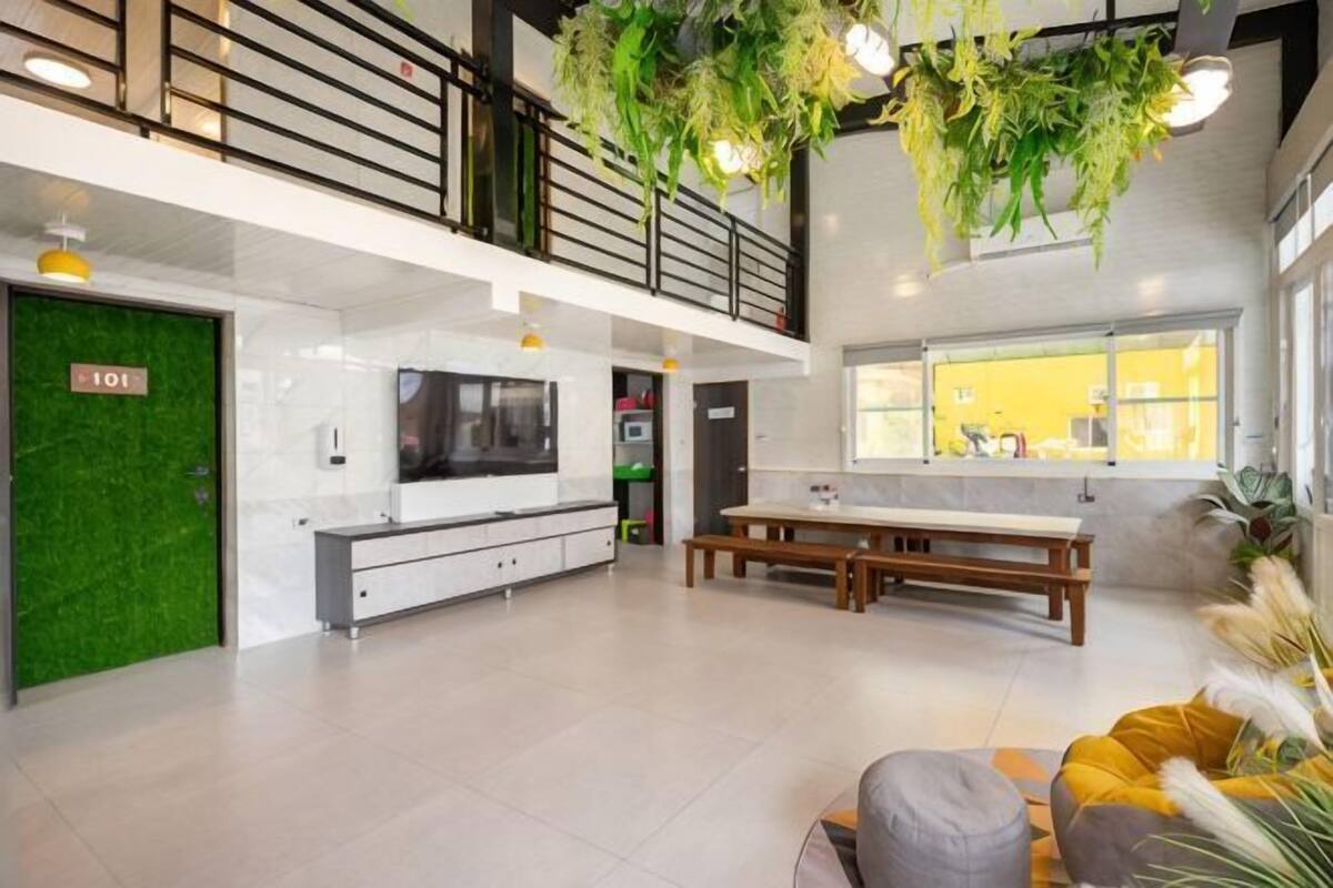 A spacious living area with a high ceiling, a green door labeled '101', a wooden bench, and a sofa with yellow cushions.