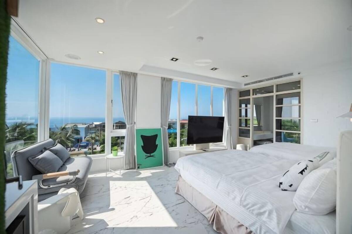 A modern bedroom with a large bed, a sofa, a TV, and a view of the ocean.