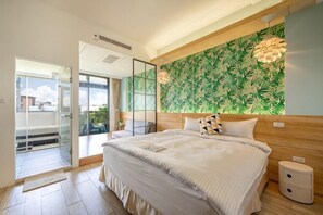 Un dormitorio con una cama grande, cabecera de madera, papel tapiz con hojas verdes y una puerta de cristal que da a un balcón.