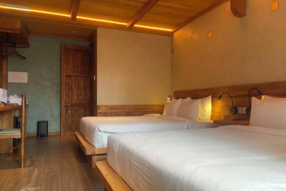 A room with two beds, wooden headboards, a bench, and a small table with a chair.