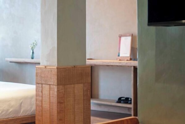 Een hotelkamer met een bed, een houten pilaar, een plank met een vaas en een aan de muur bevestigde televisie.