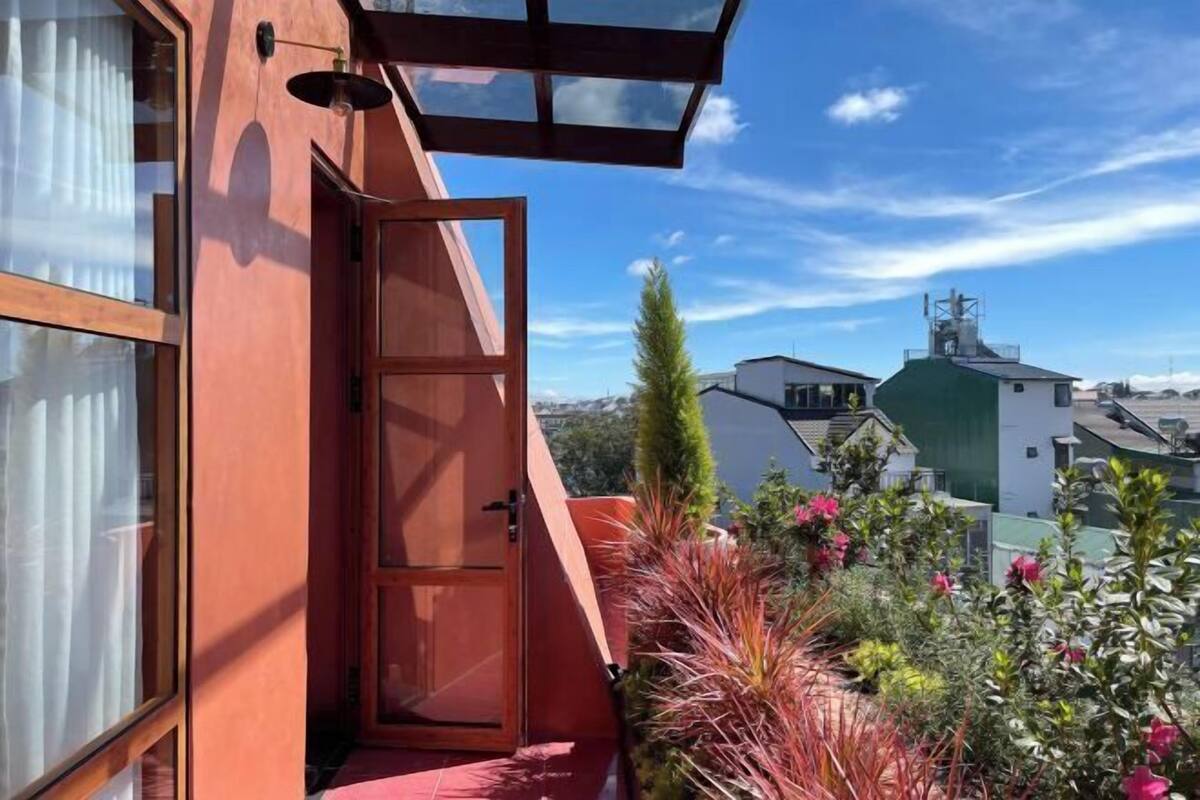 A red building with a wooden door and a small balcony with plants and flowers.