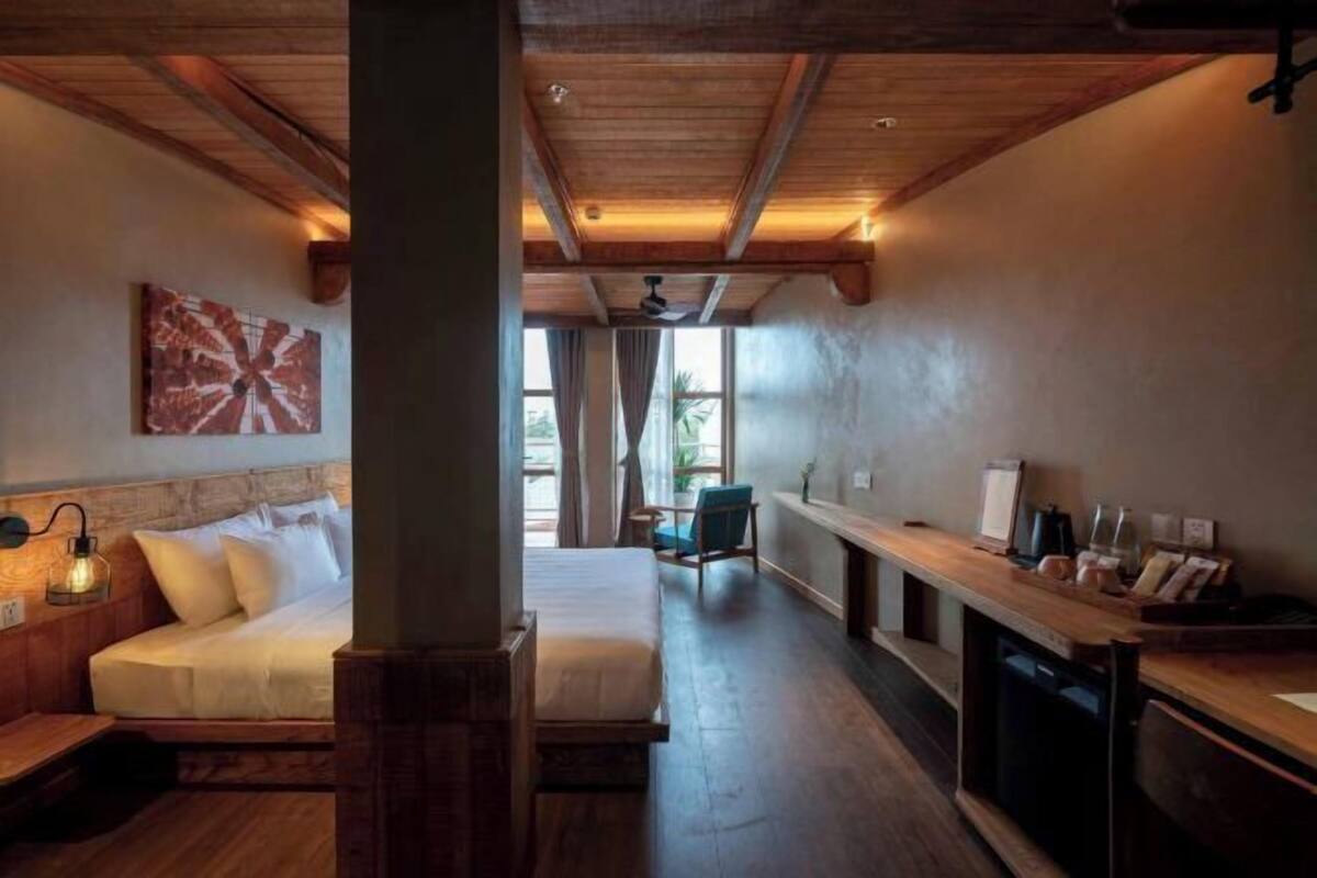 A room with a bed, a desk, and a chair. There is a window with curtains, a ceiling fan, and a wall-mounted light fixture.