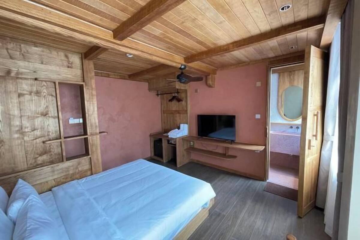 A bedroom with a wooden ceiling, a bed, a TV, and a small bathroom.