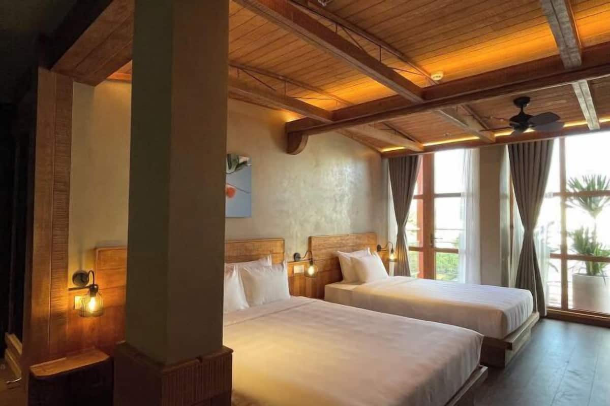 A room with two beds, wooden beams, a ceiling fan, and a window with curtains.